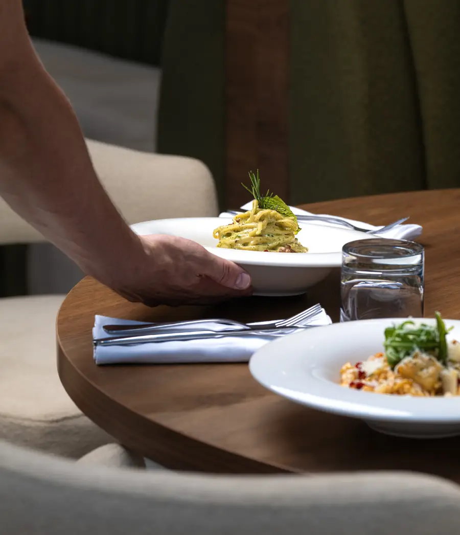 Assiette de pâtes déposée sur une table ronde en bois, banquette verte et fauteuils bouclette crème