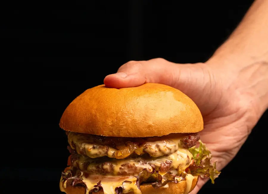 Burger au pain brioché tenu à la main sur fond noir, double steak et sauce coulante