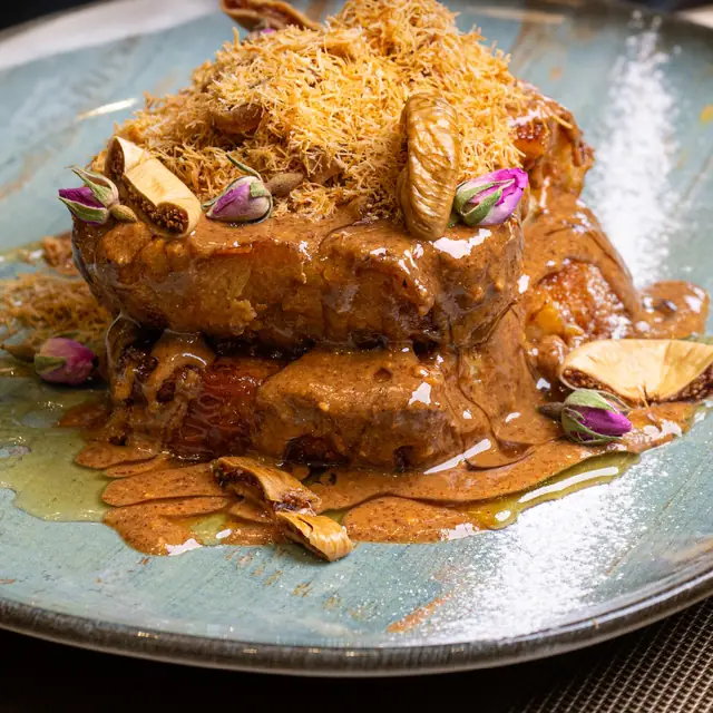 Détail du pain perdu à l'amlou : kounafa dorée, boutons de rose et figues sur assiette céladon