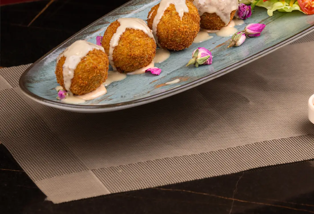Falafels nappés de sauce tahina sur plat céladon, boutons de rose séchés