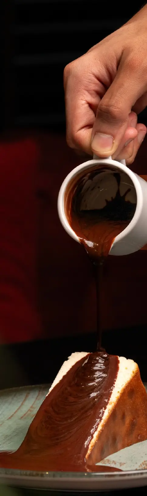 Chocolat chaud versé d'un pot blanc sur une part de gâteau, cuir rouge en fond