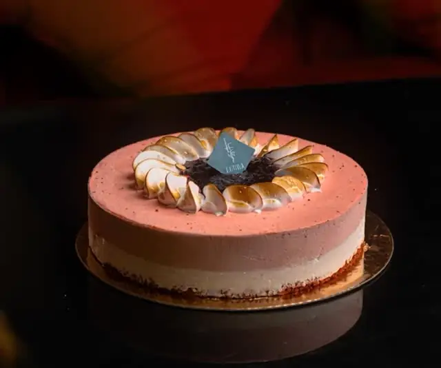 Entremets glacé rose aux pétales de meringue passés au chalumeau, sur table laquée noire