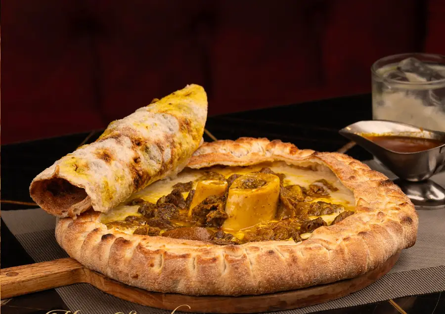 Pizza tanjia : croûte soufflée, viande confite et os à moelle au centre, msemen roulé posé sur le bord