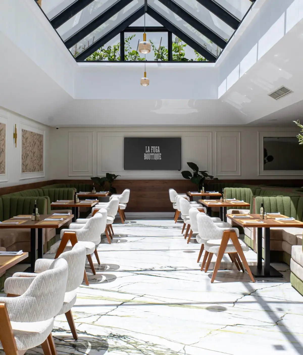 La salle de La Fuga Boutique sous sa verrière : marbre clair veiné, banquettes vertes, fauteuils crème et bois