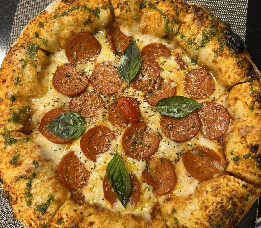 Pizza au pepperoni et au basilic frais, croûte dorée, servie coupée