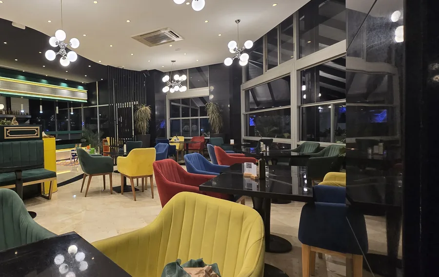 La salle : banquette de velours émeraude, fauteuils jaunes, rouges et bleus, tables laquées noires sous les lustres à globes